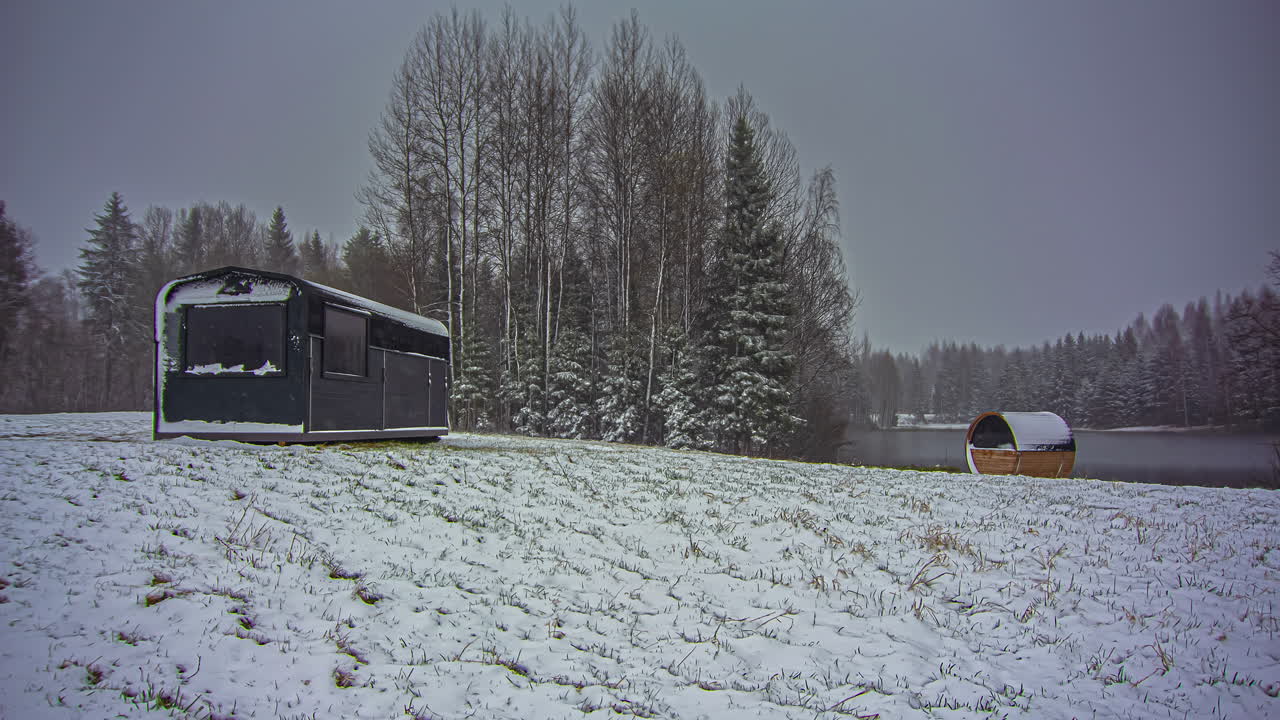 눈 덮인 겨울날 공원 리조트에서 집과 배럴 사우나를 갖춘 일출의 저속 촬영 - 자연 호수 위로 날아다니는 구름