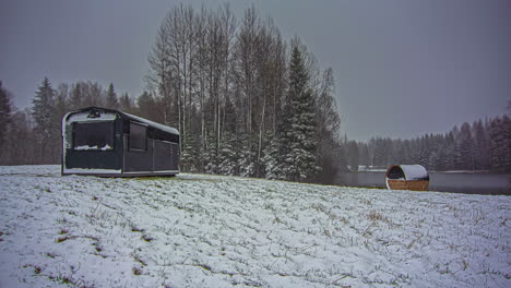 Time-lapse-shot-of-sunrise-during-snowy-winter-day-in-park-resort-with-house-and-barrel-sauna---Flying-clouds-over-natural-lake-in-backdrop