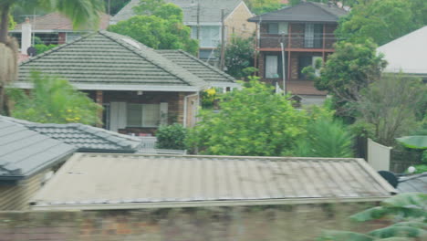 Filmando-Desde-La-Ventana-De-Un-Tren-Durante-El-Amanecer-Pasando-Por-Edificios-Y-Patios-Traseros-En-Sydney,-Australia