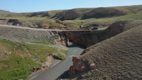 epic aerial drone shot of an old bridge near the kel-suu lake with an suv driving over it in kyrgyzstan