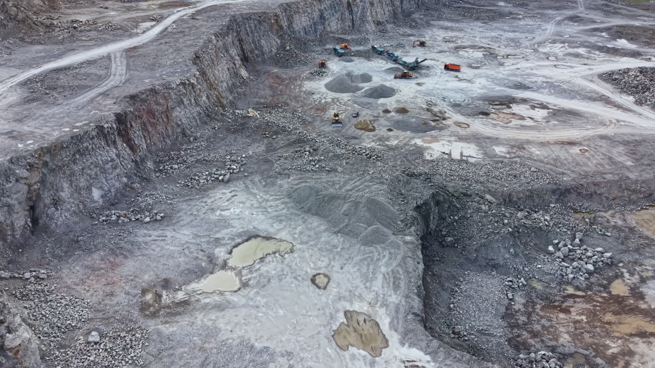 Large quarry site located in a rural area showing heavy machinery and uneven terrain with gravel and small ponds present during daylight hours