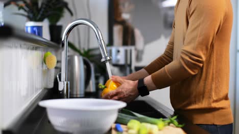 Man-washing-capsicum-with-water-under-the-tap-4k