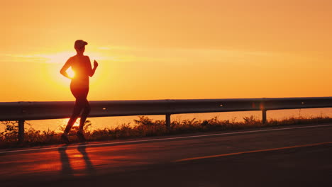 Schlanke-Sportliche-Frau,-Die-Gegen-Den-Orangefarbenen-Himmel-Und-Die-Untergehende-Sonne-Die-Straße-Entlang-Läuft-Running