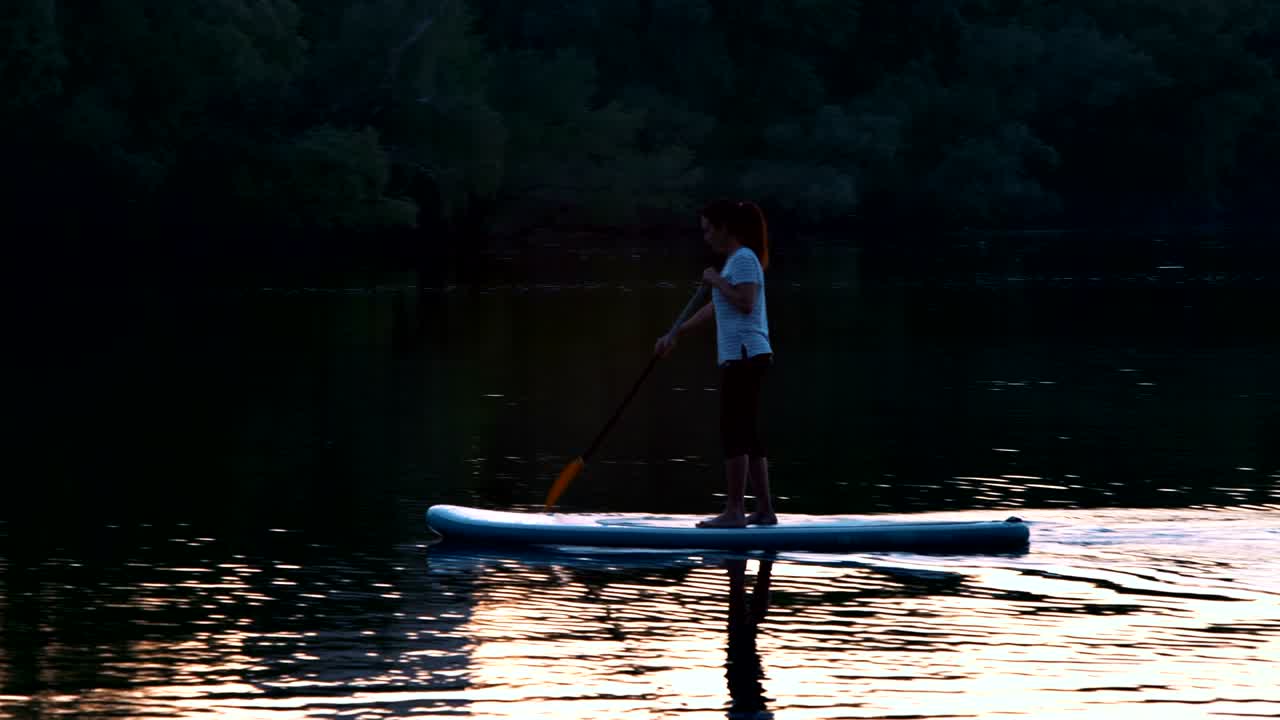 tiro largo, hermosa niña flota de pie en la sopa y filas por remos al atardecer