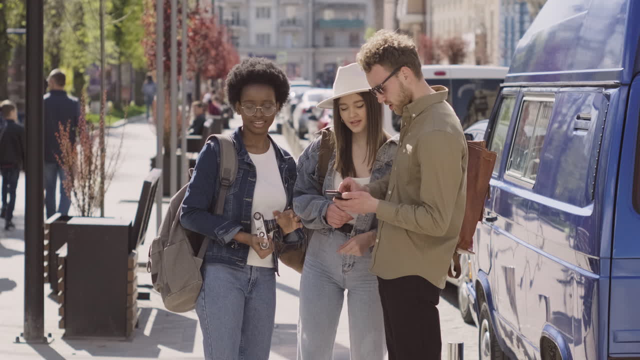 도시에 있는 세 명의 관광객, 두 명의 어린 소녀와 한 명의 젊은 남성이 휴대폰의 주소를 보고 있습니다.
