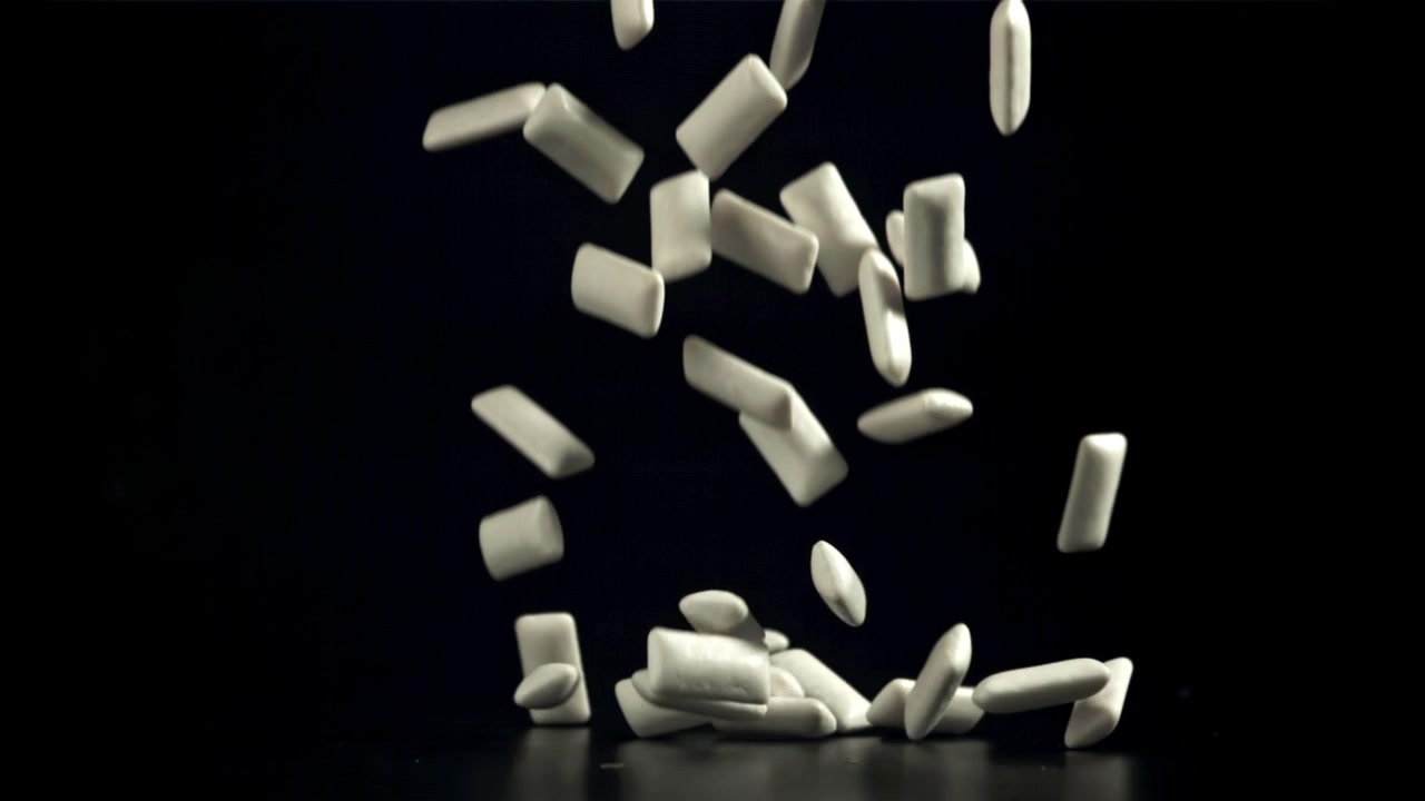 White Chewing Gum Pellets Falling in Slow Motion on Black Background