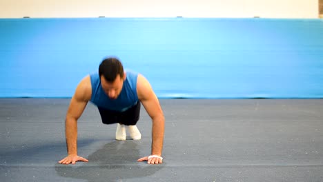 a guy doing a special kind of push up in a top-side-front view still shot inside a gymnastics gym