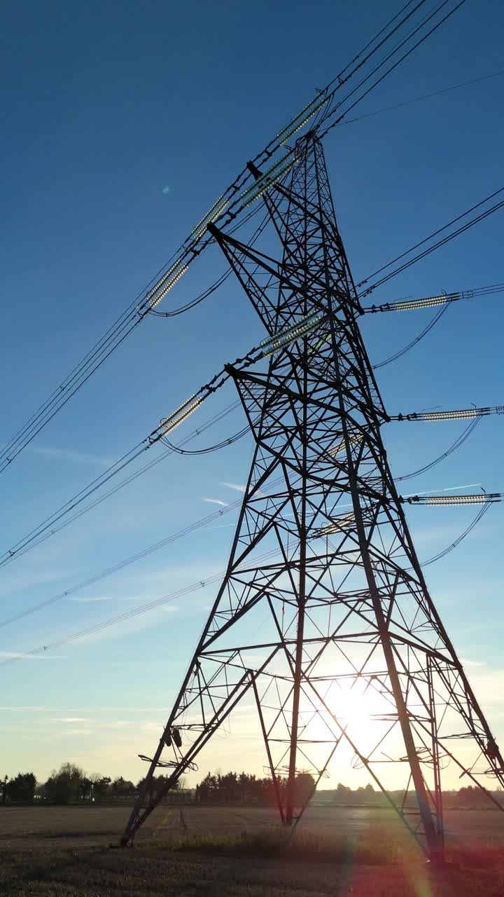 Industrial silhouette of a power pylon under a glowing sunset horizon in the British landscape representing national energy infrastructure and supply