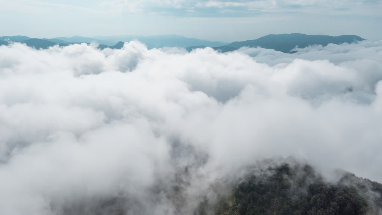 Thick clouds blanket the mountain range creating a mystical and serene aerial view