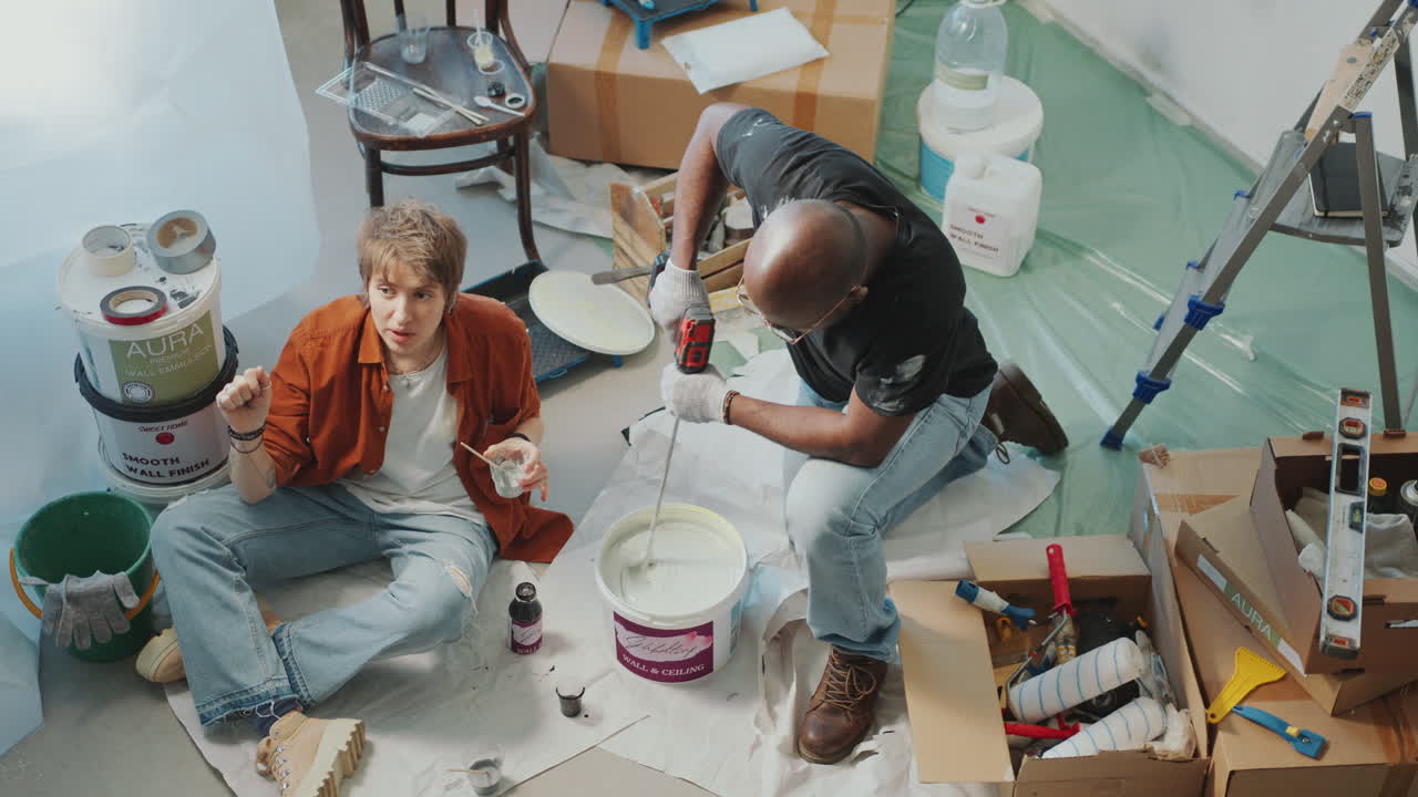 Woman Talking with Husband Stirring Paint with Drill in Room under Renovation