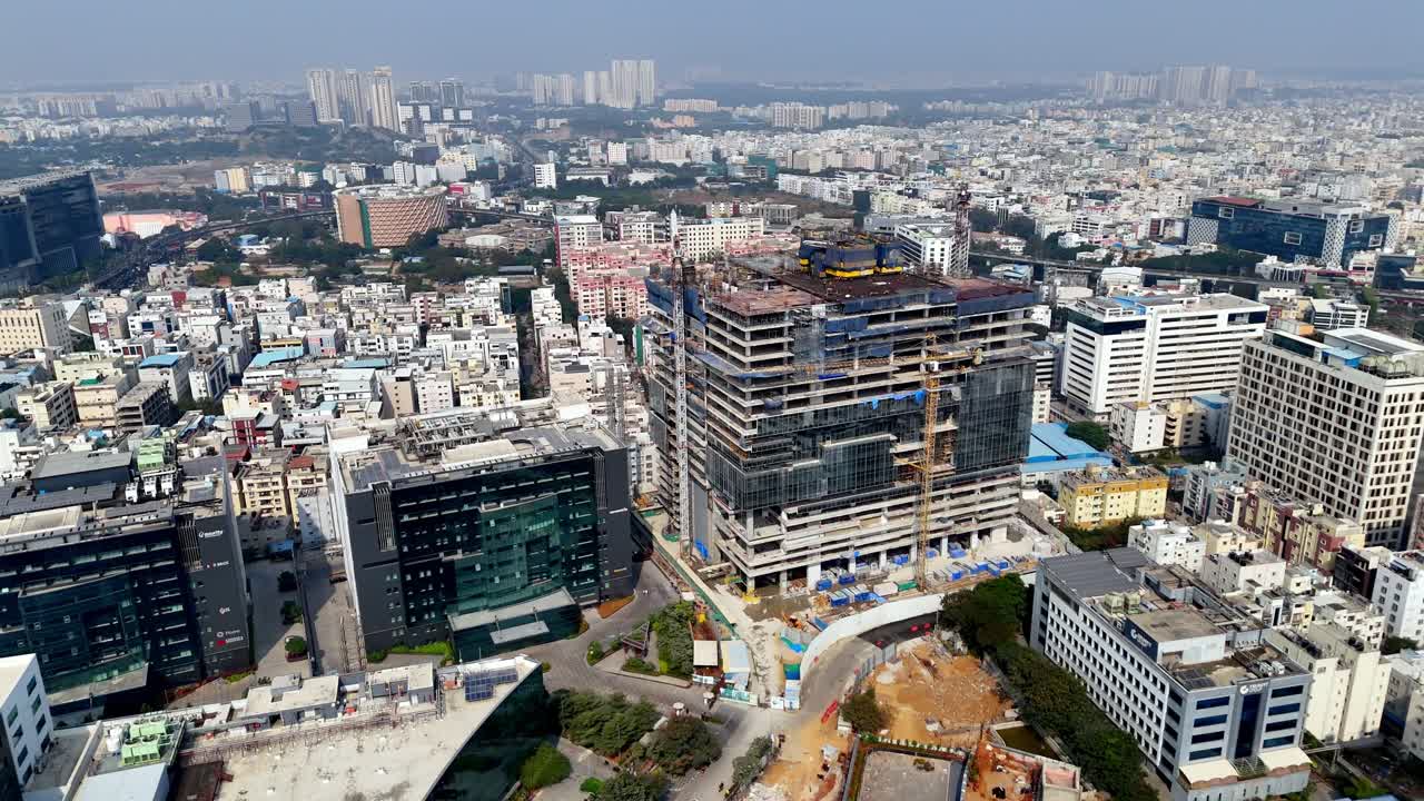 Aço, vidro e guindastes moldam o futuro—uma vista aérea de uma torre icónica em construção no próspero distrito comercial da HITEC City. Cenário urbano denso em transição para um centro de cidade moderno.