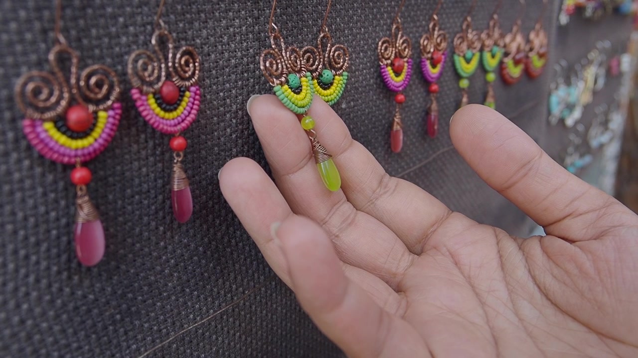 Hand Touching Handmade Beaded Earrings at a Market Stall