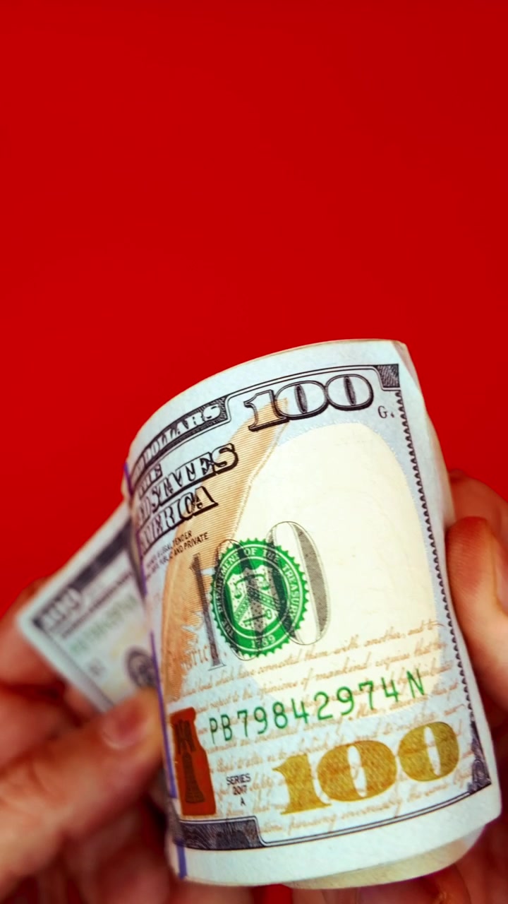 B-roll verticale 9:16: mani che sventagliano banconote da 100 dollari su sfondo rosso. Concetto per denaro veloce, motivazione alla ricchezza, transazione illegale, pagamento di stipendio, affari sul dark web e successo finanziario.