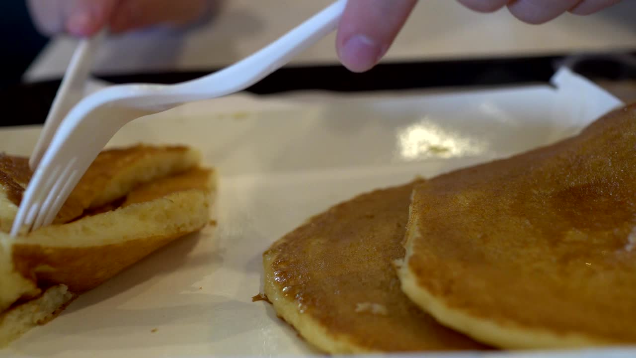 아이의 손에 칼과 포크를 고 아이가 팬케이크를 잘라내고 있습니다.