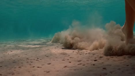 under water scene of little girl jumps on seabed raising clouds of sand in transparent water