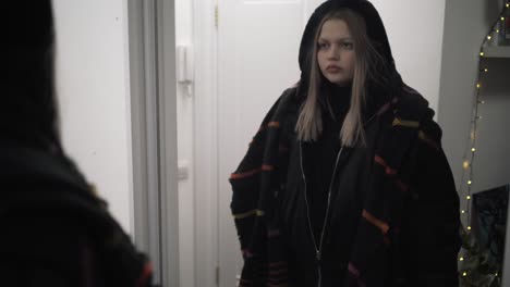 teenager looking at themselves in a mirror while adjusting a jacket and scarf