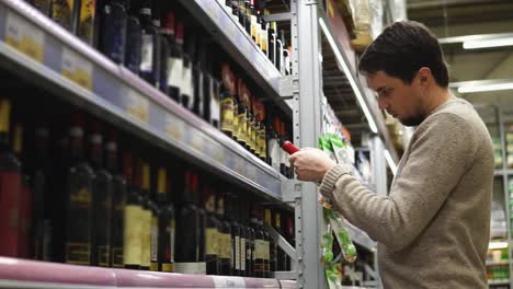 hombre eligiendo vino rojo en una tienda de comestibles