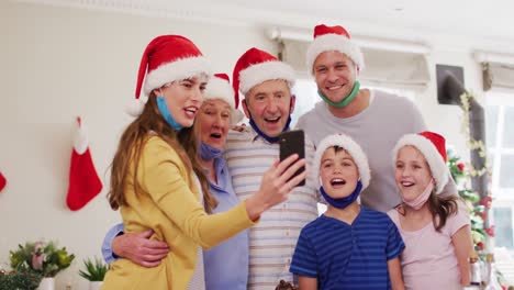 familia caucásica con sombreros de santa y máscaras faciales alrededor de sus cuellos tomando una selfie juntos usando