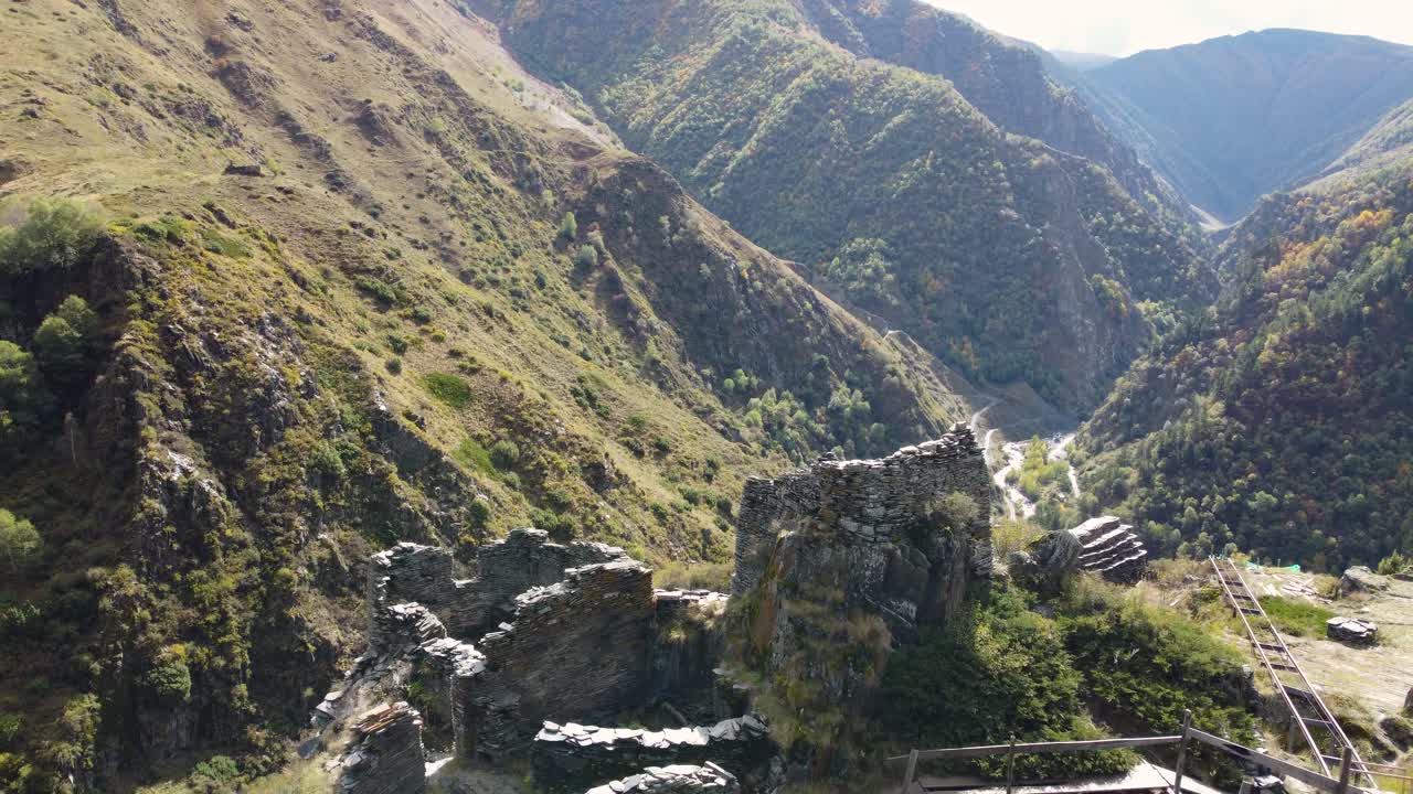 Dynamic drone fly over a mountain range winding around Mutso village historical ruins on rocky landscape, Khevsureti, Mtskheta-Mtianeti, Georgia