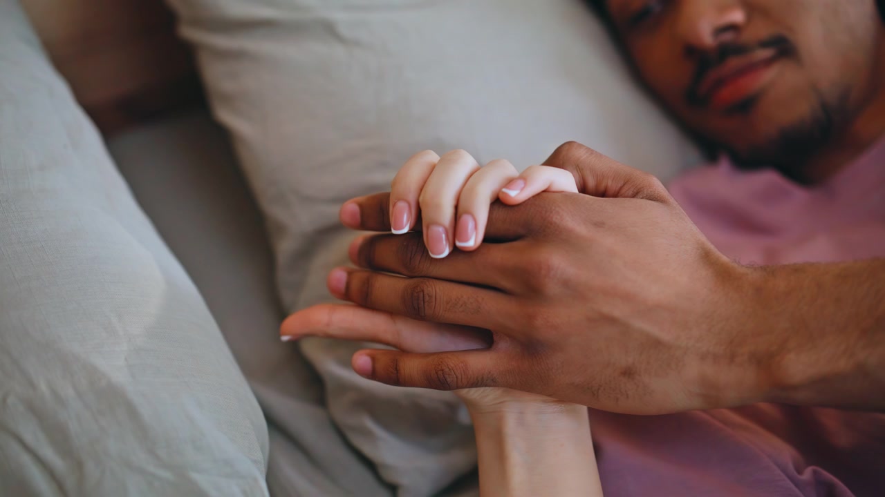Man holding girlfriend hand bed close up. Multiracial lovers resting bedroom.