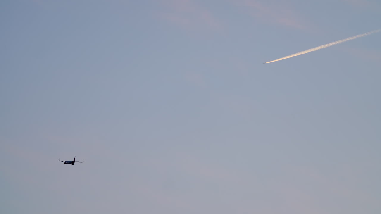 Due aerei nel cielo, un aereo di linea e una scia di condensazione al tramonto.