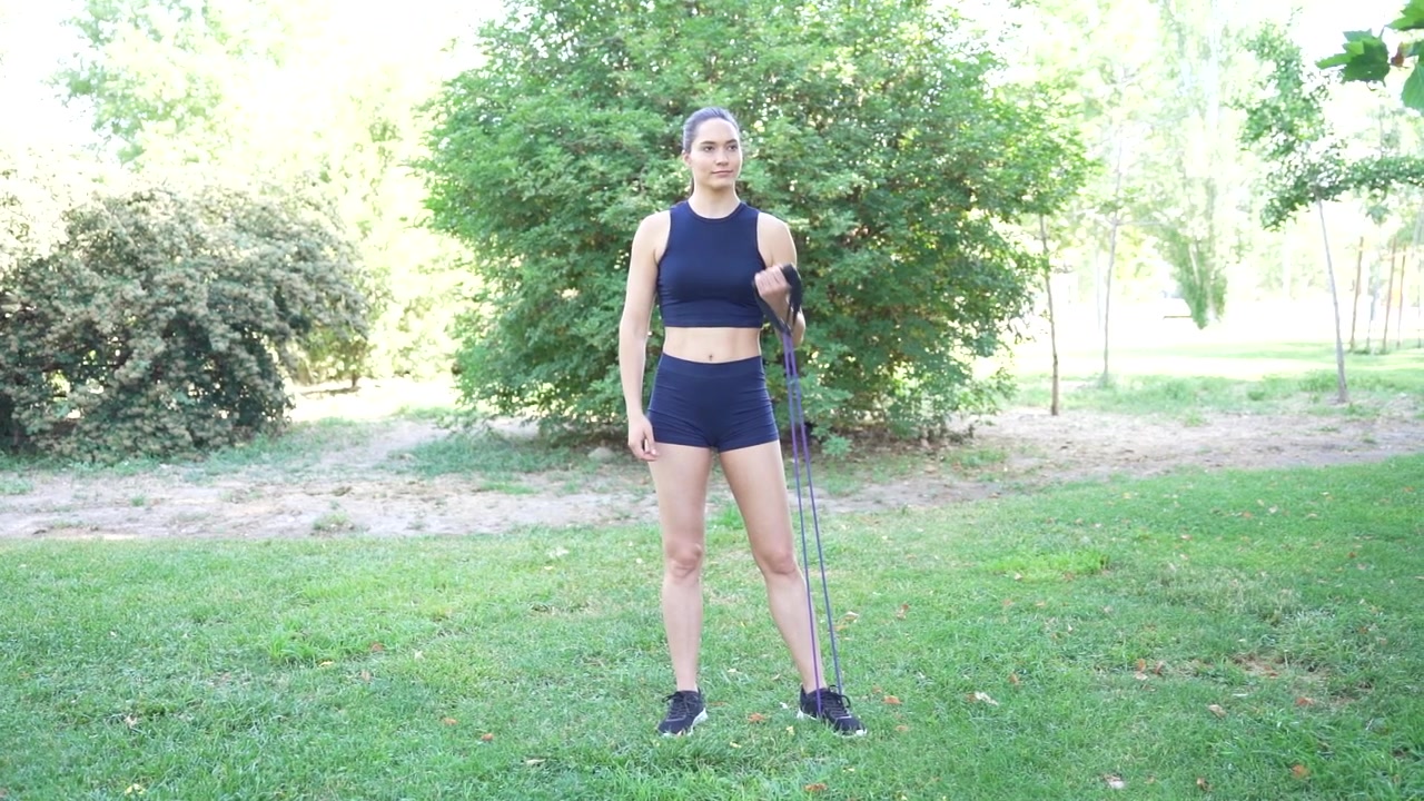 Una donna si allena con una fascia di resistenza in un parco, godendosi l'esercizio all'aperto.