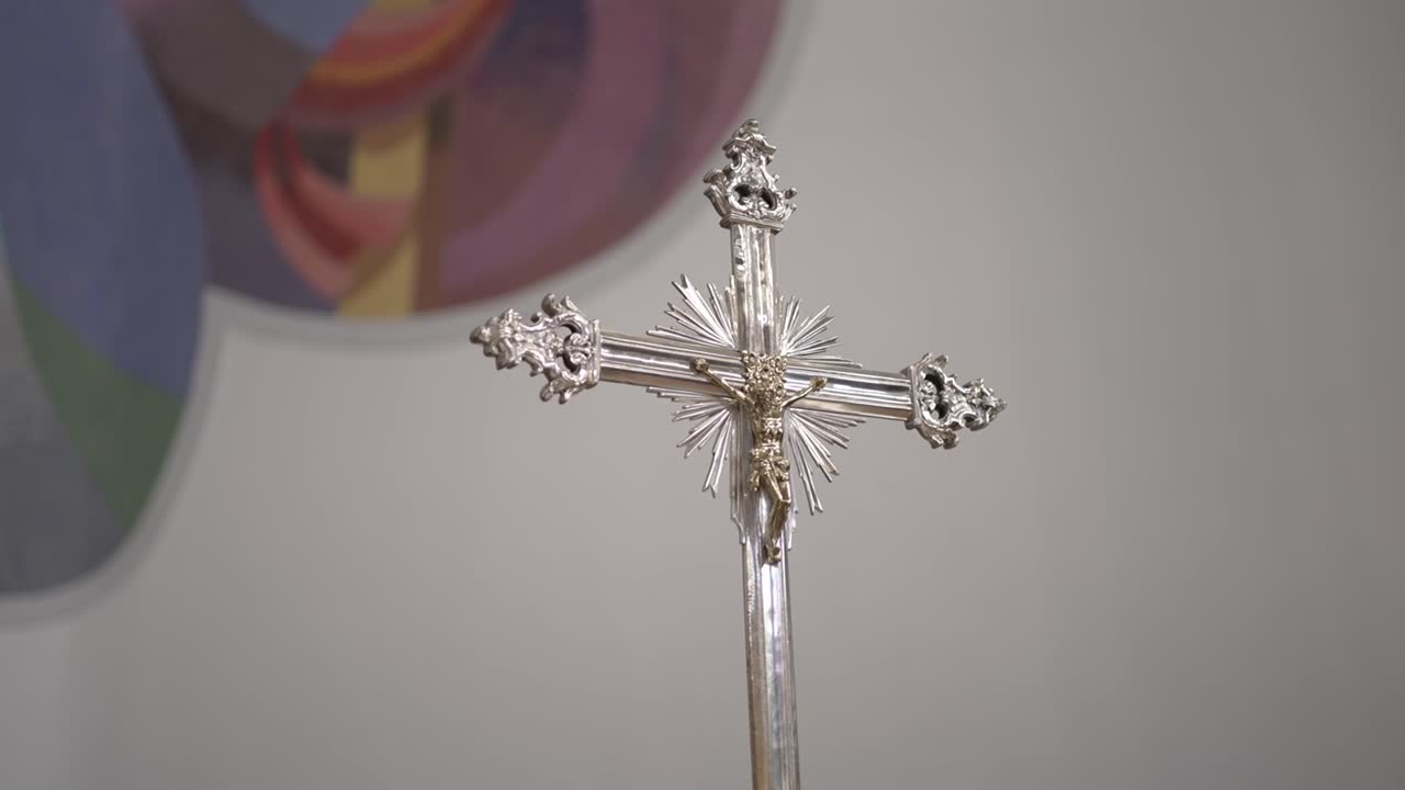 Close-up silver crucifix with detailed design and figure of Christ against soft wall and mural background