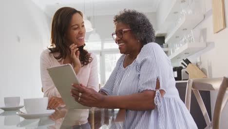 Senior-mixed-race-woman-using-a-digital-tablet-with-her-daughter,-in-social-distancing-