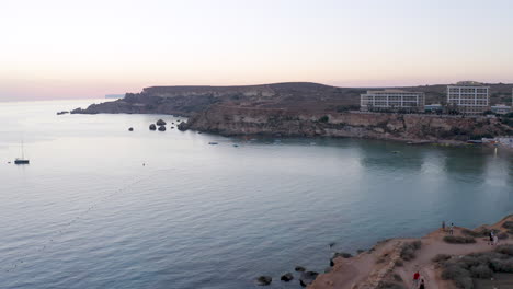 Flag-of-the-Maltese-order-waving-on-a-tower-above-a-bay,sunset,aerial