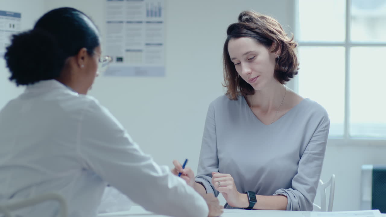 Woman Signing Medical Agreement and Speaking with Doctor in Clinic