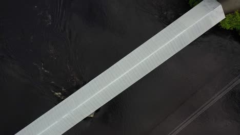 Top-down-drone-shot-of-the-steel-roof-of-a-covered-bridge-over-a-dark-river-with-water-flowing-quickly-under-it-in-Wakefield-Quebec-Canada