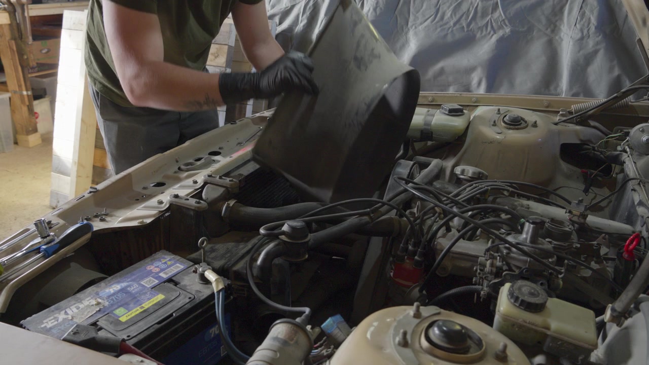 A mechanic removes the fan shroud and cooling fan from an old gasoline engine, exposing components during hands-on automotive maintenance.