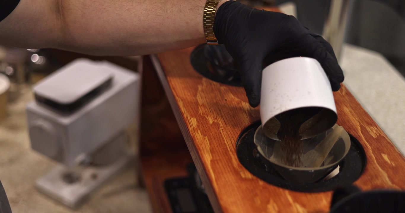 Un barista versa caffè macinato fresco in un filtro di carta all'interno di un dripper per caffè filtro, inquadratura media.