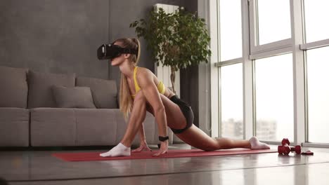 Sportive-girl-with-perfect-muscular-body-wears-VR-mask-during-her-home-work-out-at-living-room.-Girl-in-a-mask-doing-legs