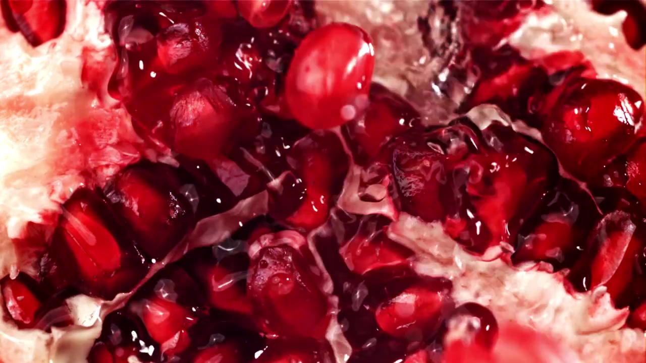 Slowmotion nærbillede af granatæblekerner, der sprøjter med vand