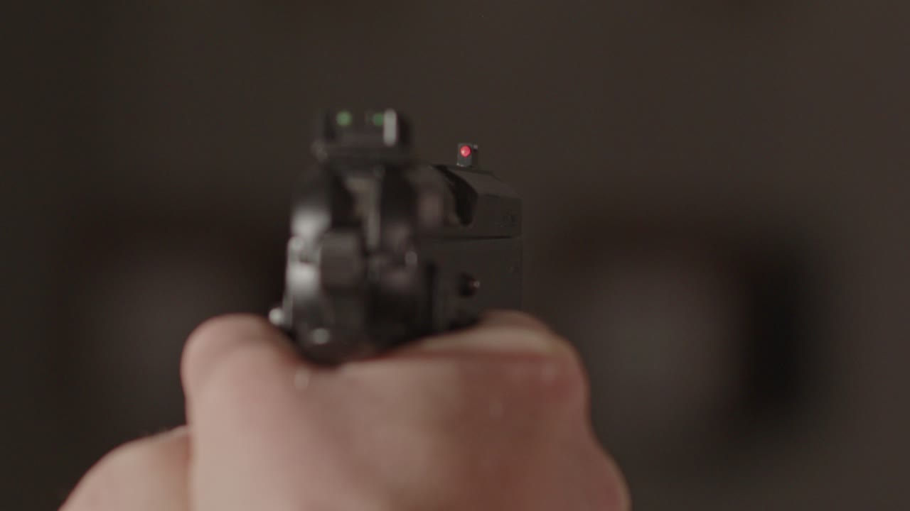 через плечо пистолет, направленный на неясного субъекта в темном здании