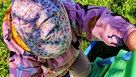 happy toddler climbing green slide steps in colorful jacket and spring sun