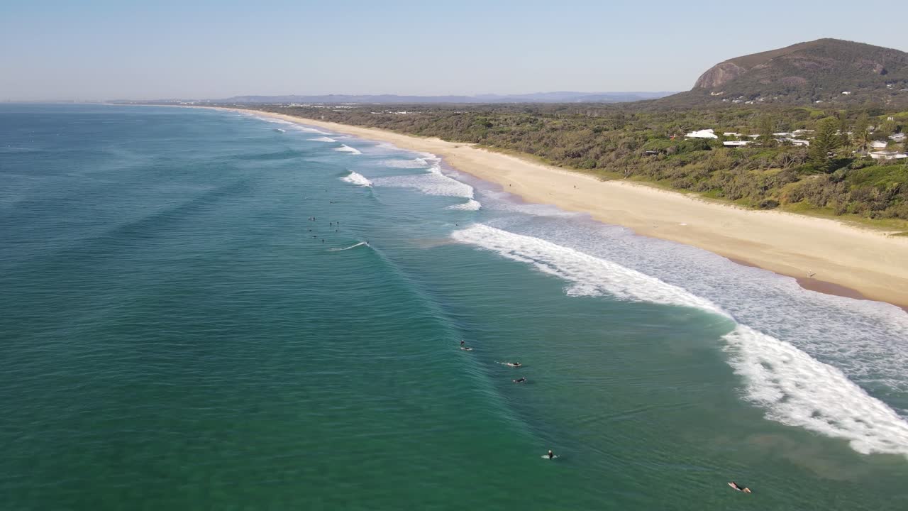 Drone aerial moving towards surfers at a clear blue water beach on a sunny day