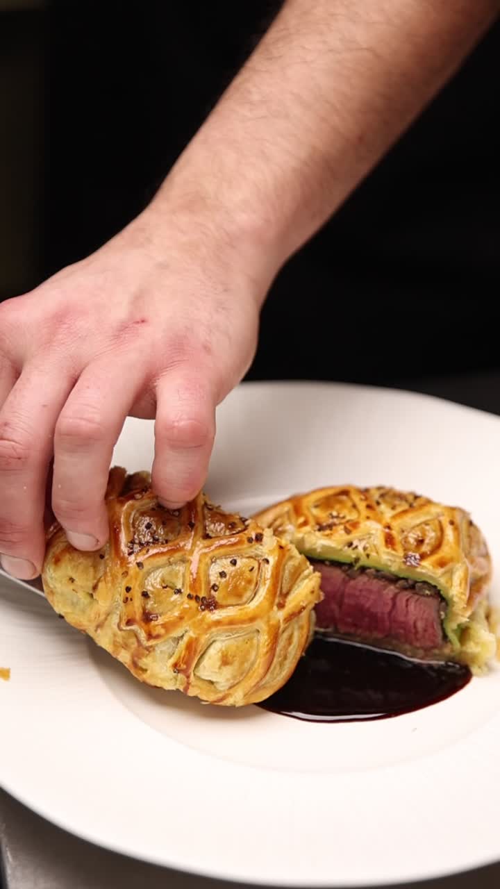 Chef che serve un filetto alla Wellington gourmet con salsa su un piatto bianco
