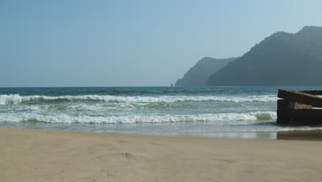 Waves-gently-crashing-on-shore-line-with-mountains-in-the-background-in-slow-motion