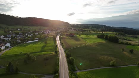 Una-Vista-Aérea-Panorámica-De-Una-Carretera-Que-Atraviesa-Exuberantes-Campos-Verdes-En-Greifensee,-Suiza