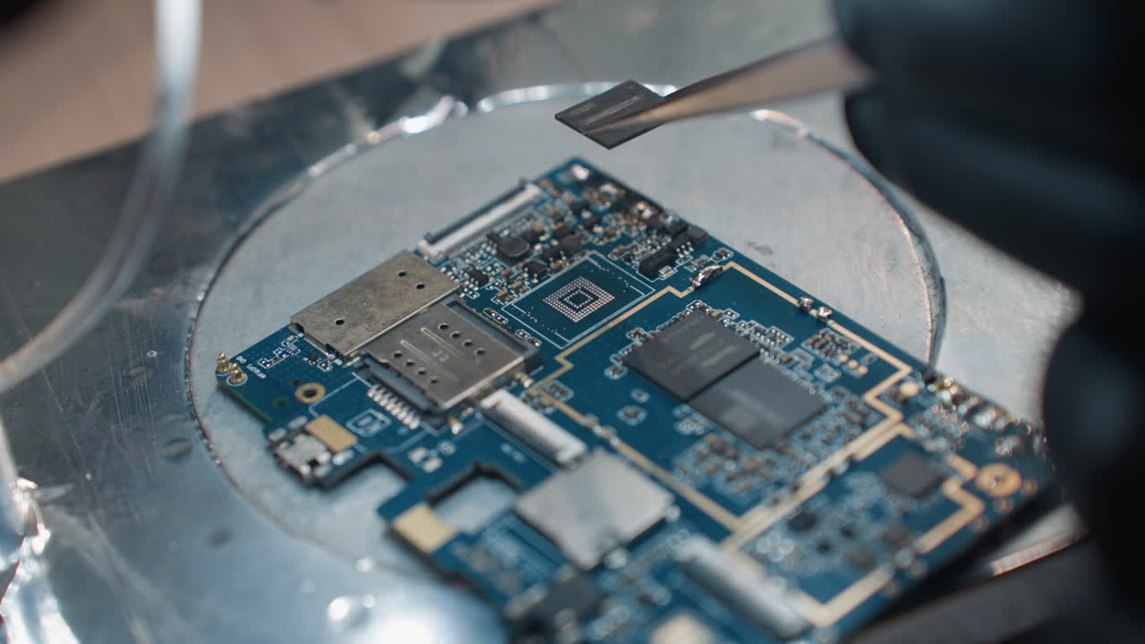 una vista de cerca de las manos con guantes de un técnico usando una herramienta de precisión para trabajar en una placa de circuitos bajo un microscopio para eliminar un chip
