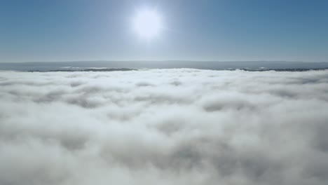 Clouds-and-sun,-drone-rises-above-thick-fog-over-the-beautiful-ocean-of-clouds-at-sunrise