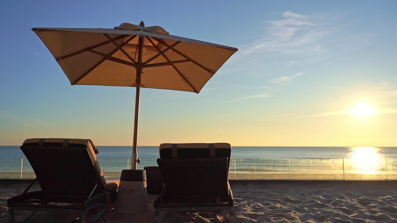 Due lettini e un ombrellone su una spiaggia vuota, riflesso del sole al tramonto sull'acqua del mare