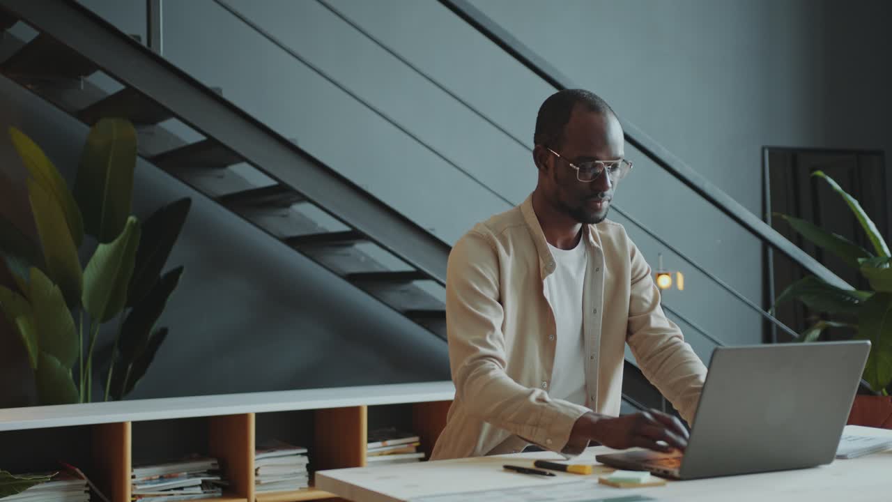 Black Businessman Writing Business Report on Laptop in Stylish Office