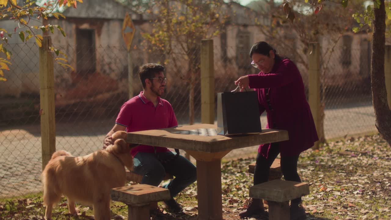 A couple with their Golden Retriever dog enjoying leisure time at an outdoor park with a chess table