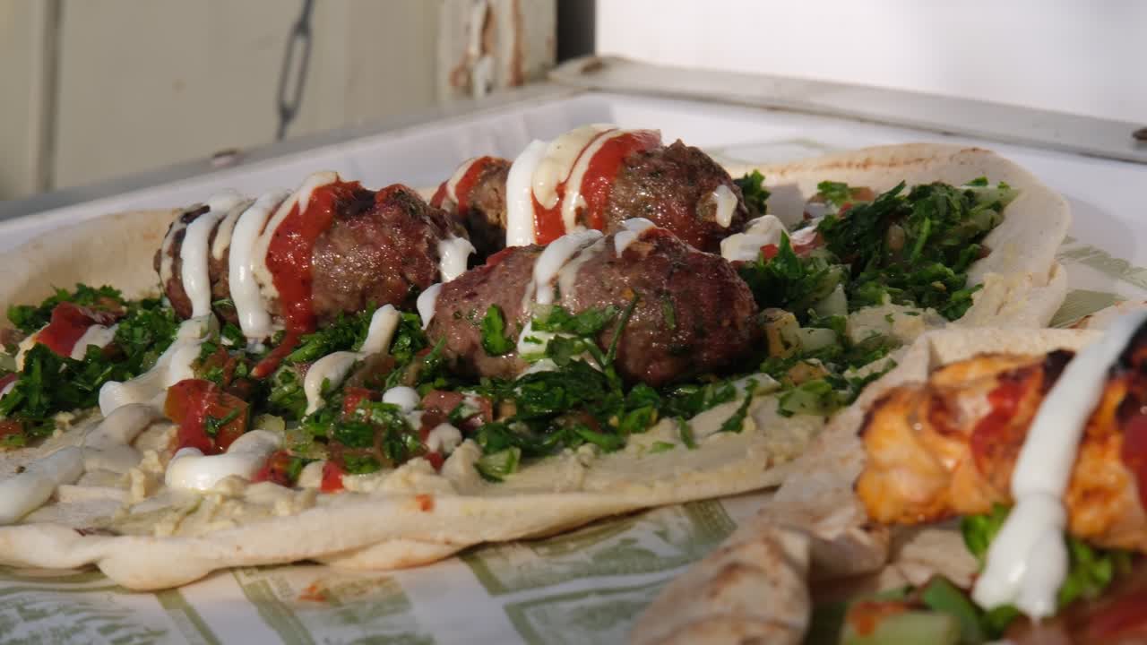Primo piano appetitoso di kebab di pollo grigliato e polpette serviti in pane azzimo con insalata fresca e salsa cremosa. Perfetto per immagini di street food, cibo da asporto o ristoranti fast casual.