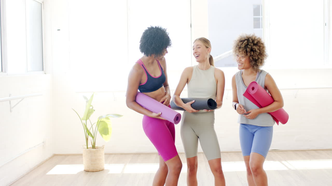 tres mujeres están de pie en un estudio de yoga brillante, sosteniendo esteras