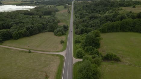 aerial shot of the long highway with driving cars surrounded by green lush trees from both sides