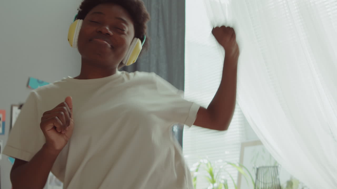 Donna afroamericana entusiasta con le cuffie che balla a casa.